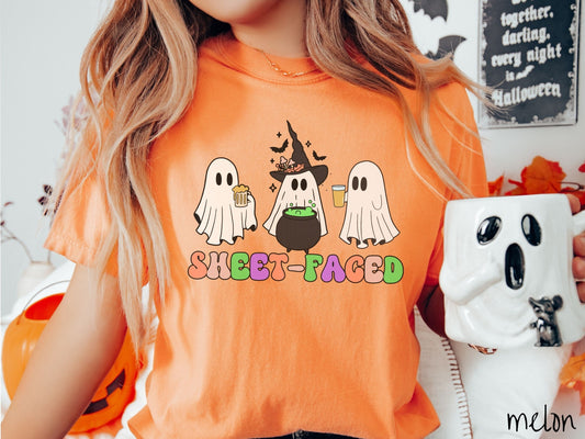A woman wearing a vintage, melon colored Comfort Colors t-shirt with the text Sheet-Faced in colorful font across the front. Above are three white ghosts drinking beers and standing around a black cauldron with a bubbling green liquid in it.