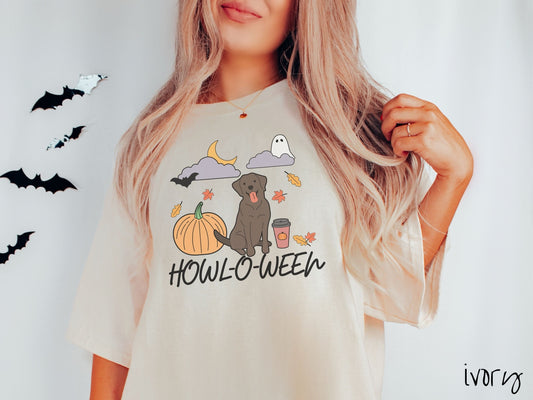 A woman wearing a vintage, ivory colored Comfort Colors t-shirt with the text Howl-O-Ween across the front. Above are a smiling Chocolate Lab dog, an orange pumpkin, a pumpkin-spiced latte, fall leaves, and a ghost and bat in the air.
