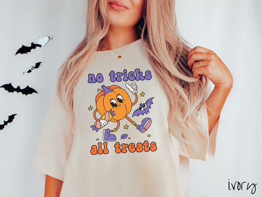 A woman wearing a cute, vintage ivory colored Comfort Colors T-shirt with the text no tricks all treats in purple and orange font. Below is a female pumpkin walking with candy in its hand wearing purple shoes and a purple bat in the background.