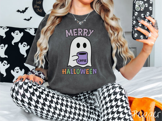 A woman wearing a cute, vintage pepper colored Comfort Colors t-shirt with the text Merry Halloween in purple, orange, and green font. There is a cute ghost holding a coffee mug in between the text.