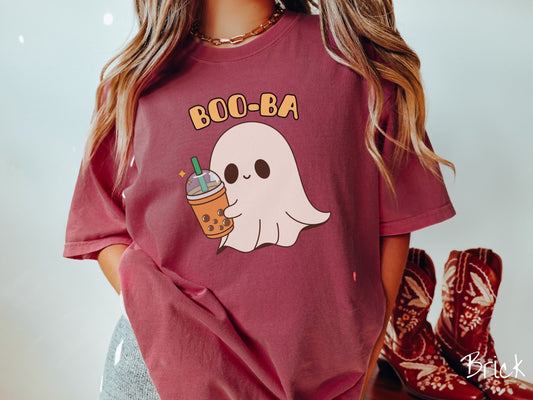 A woman wearing a cute, vintage brick colored Comfort Colors T-shirt with the text Boo-Ba in yellow font across the top. Below is a little smiling white sheet ghost holding a light brown boba tea in a plastic to-go cup.