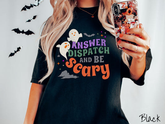 A woman wearing a cute, vintage black colored Comfort Colors T-shirt with the text Answer Dispatch and Be scary in colorful font. There are orange-eyed white ghosts flying around and black bats and twinkling stars in the sky.