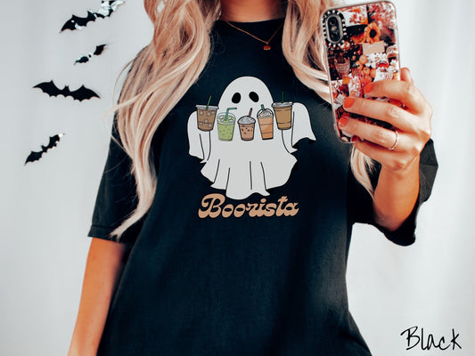 A woman wearing a cute, vintage black colored Comfort Colors T-shirt with the text Boorista along the bottom. Above is a white ghost holding an iced coffee, a green matcha tea, a frappuccino, a pumpkin spiced latte, and an iced mocha latte.