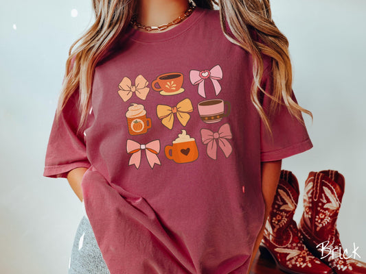 A woman wearing a cute, vintage brick colored Comfort Colors T-shirt with a grid of pictures of an orange bow, an orange tea cup, a pink bow, an orange pumpkin-spiced latte, a yellow bow, a pink coffee cup, a pink bow, and an orange coffee drink.