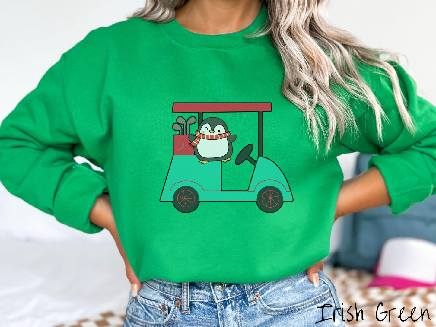A woman wearing a cute irish green colored sweatshirt with smiling penguin driving a green golf cart and waving with both hands.