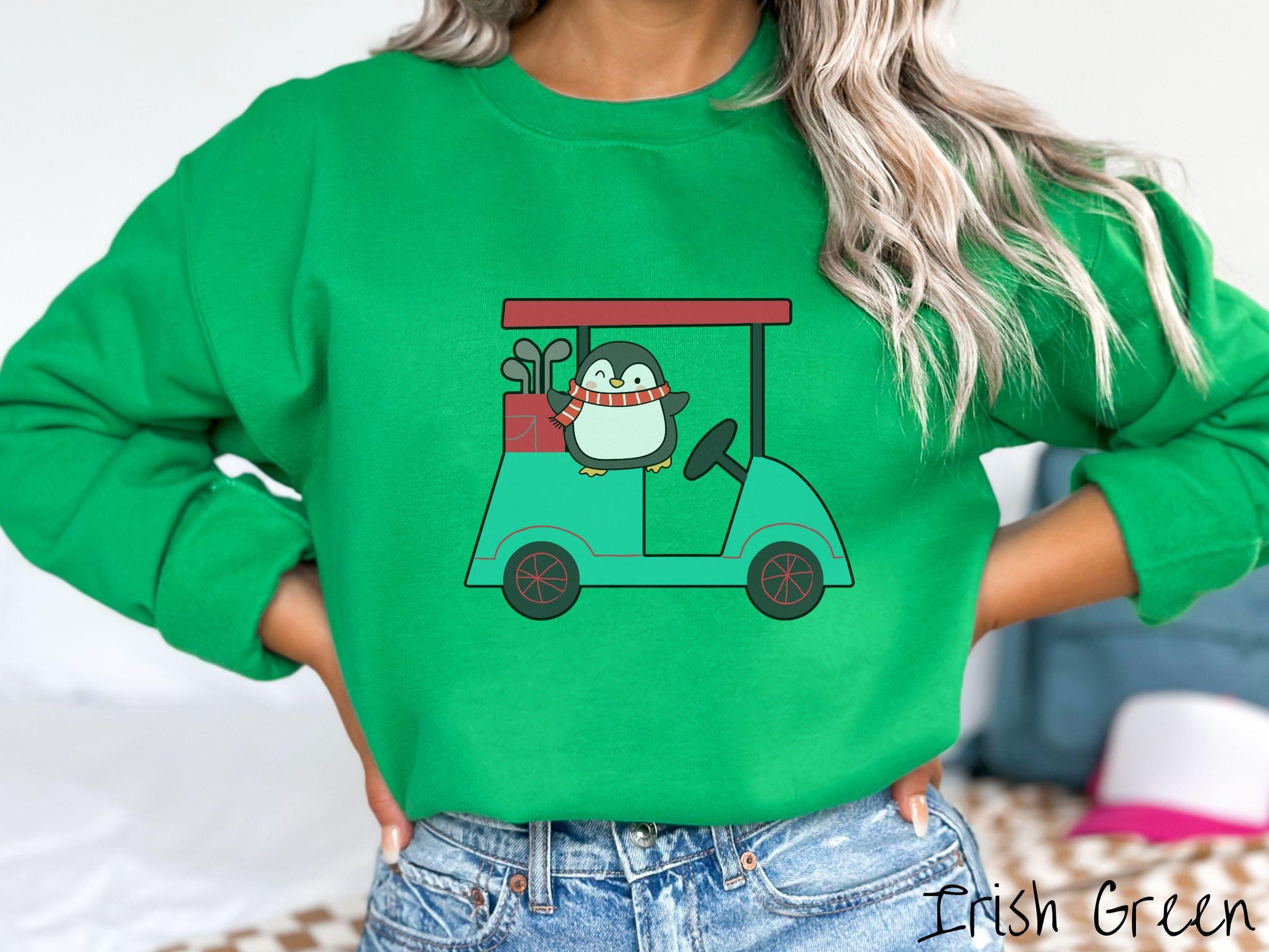 A woman wearing a cute irish green colored sweatshirt with smiling penguin driving a green golf cart and waving with both hands.