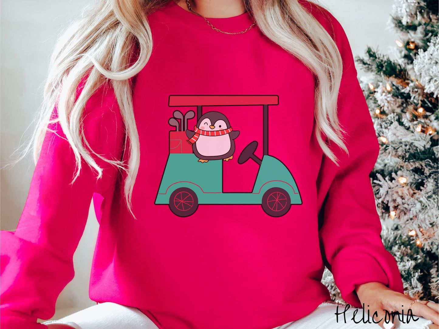A woman wearing a cute heliconia colored sweatshirt with smiling penguin driving a green golf cart and waving with both hands.
