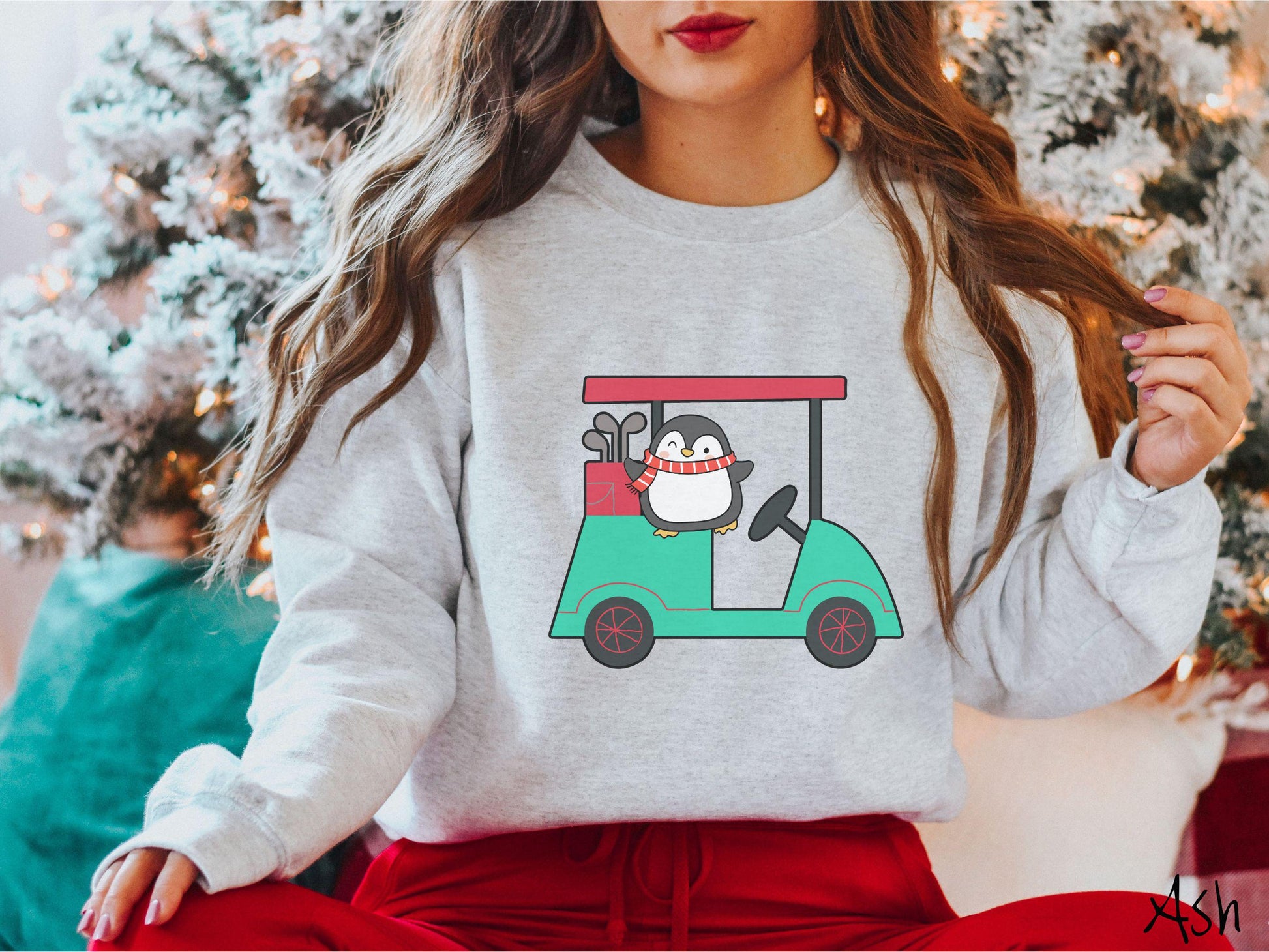 A woman wearing a cute ash colored sweatshirt with smiling penguin driving a green golf cart and waving with both hands.