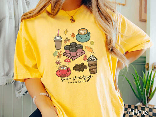 A woman wearing a cute, vintage citrus colored Comfort Colors T-shirt with the text so very thankful. Above are an iced coffee, four to-go cup coffees, a latte, a frappucino, coffee beans, mushrooms, and fall leaves scattered around.