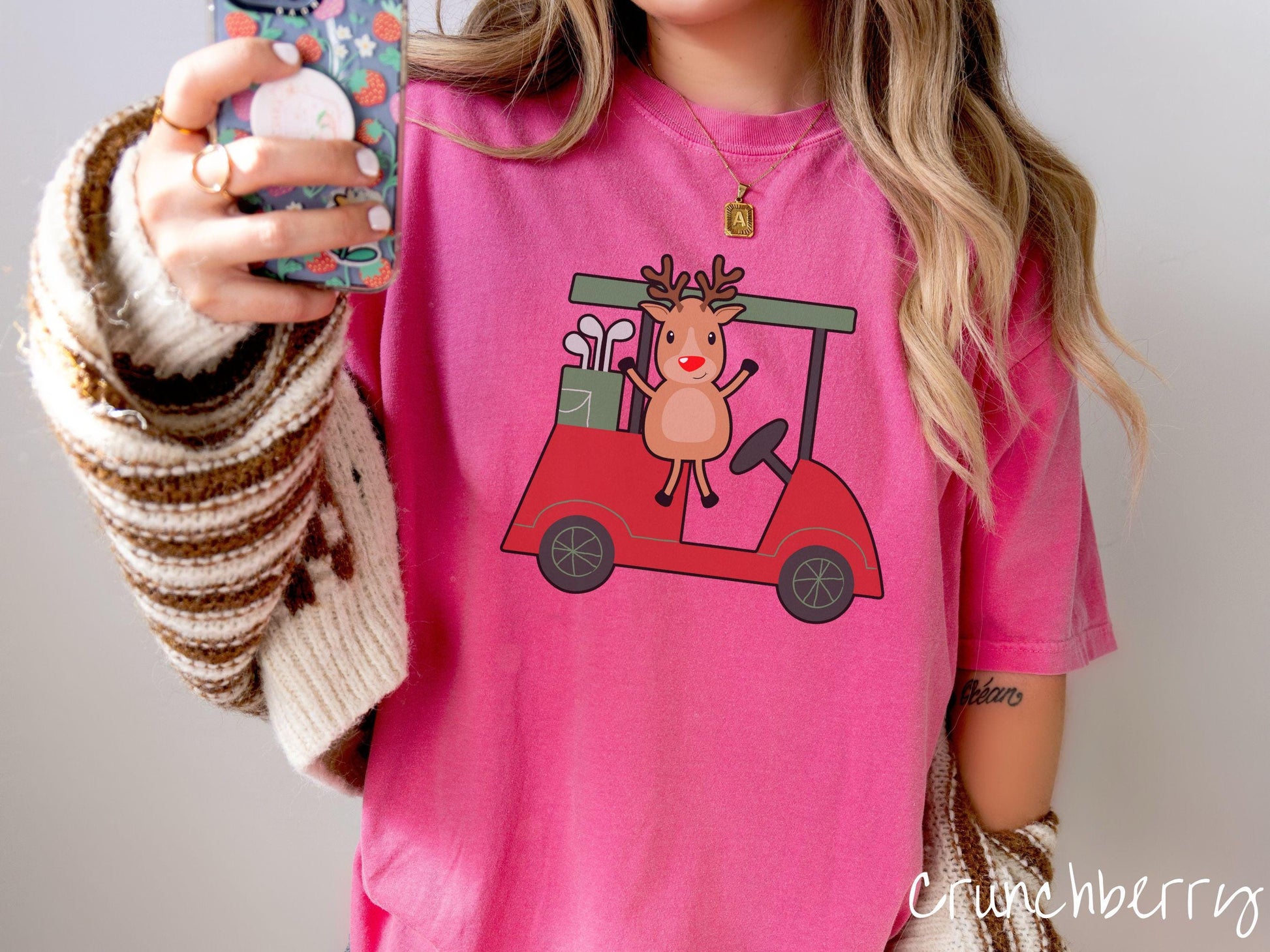 A woman wearing a cute crunchberry colored shirt with smiling reindeer driving a red golf cart and waving with both hands.