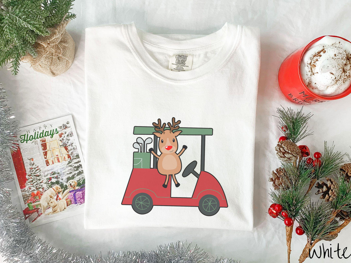 A woman wearing a cute white colored shirt with smiling reindeer driving a red golf cart and waving with both hands.