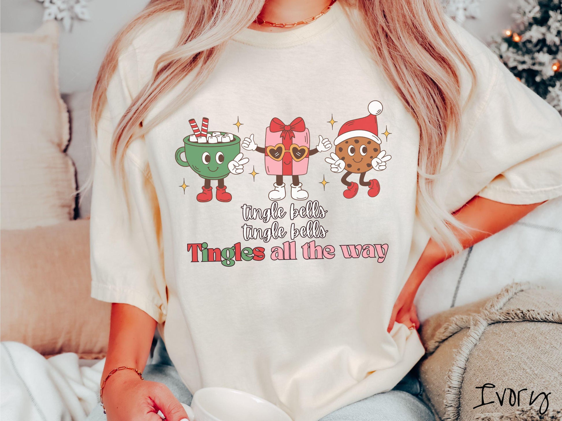 A cute, vintage ivory colored Comfort Colors T-shirt with the text tnigle bells, tingle bells, tingles all the way. Above are a green cup of hot cocoa holding a peace sign, a red present holding two thumbs up, and a cookie holding up peace signs.