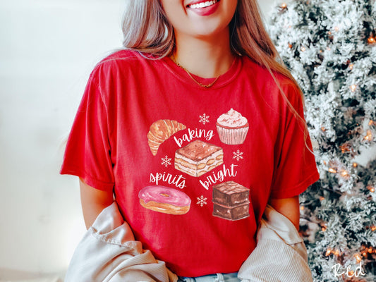 This vintage red colored Comfort Colors T-shirt features the text &#39;baking spirits bright&#39; in white cursive font, accompanied by cute dessert illustrations and white snowflakes.