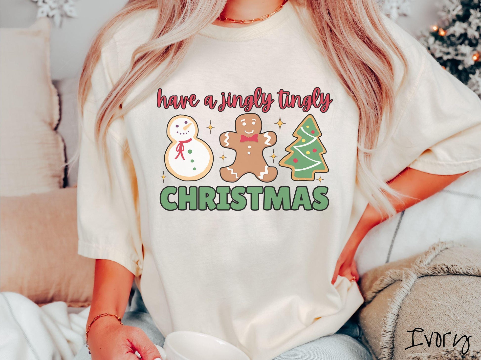 A vintage ivory colored Christmas Comfort Colors t-shirt featuring a snowman iced cookie, a gingerbread man cookie, and a Christmas tree cookie. The text reads 'have a jingly tingly Christmas' in red and green font.
