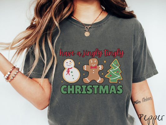 A vintage pepper colored Christmas Comfort Colors t-shirt featuring a snowman iced cookie, a gingerbread man cookie, and a Christmas tree cookie. The text reads 'have a jingly tingly Christmas' in red and green font.