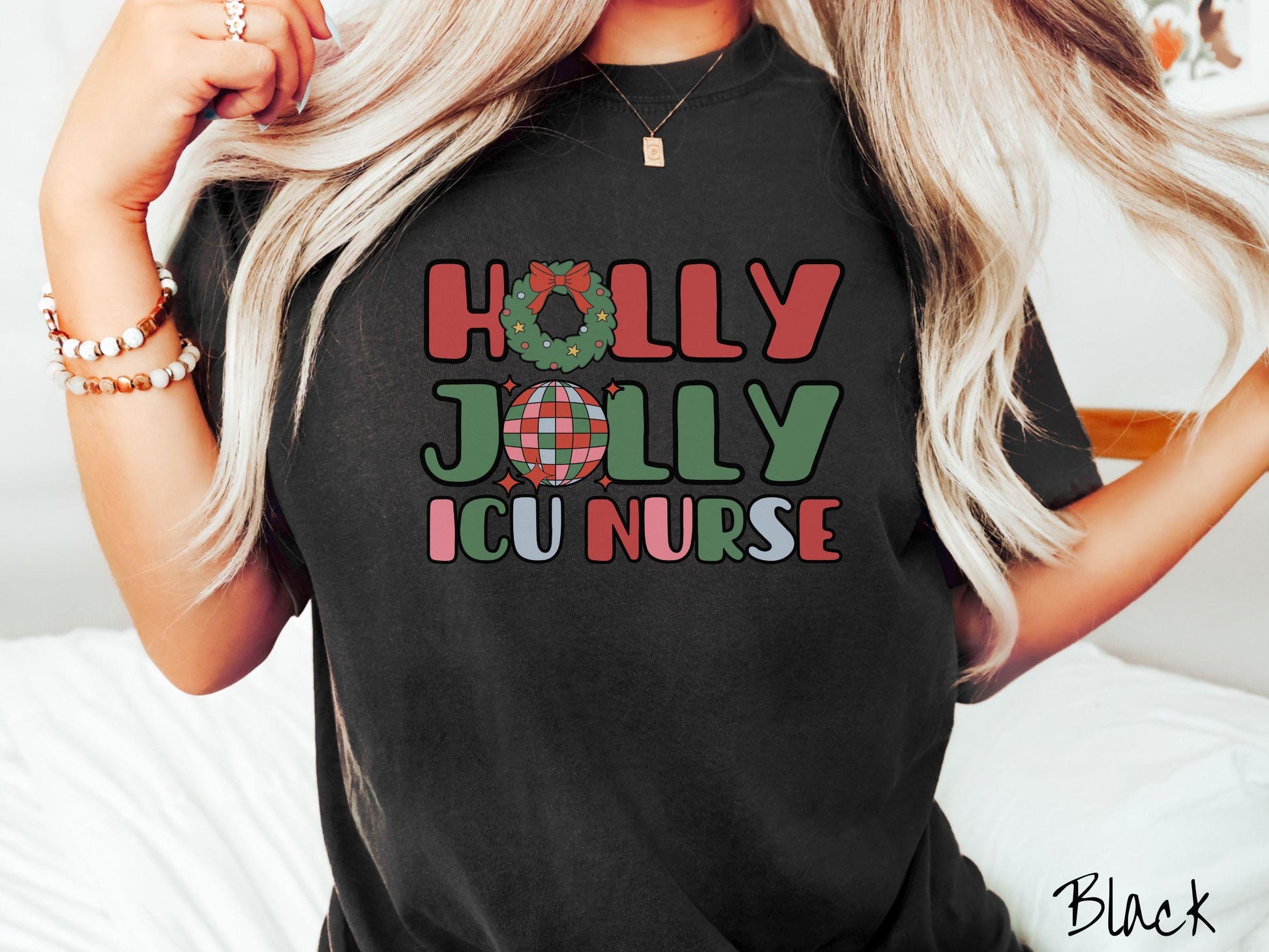 A woman wearing a cute, vintage black colored Comfort Colors T-shirt with the text Holly Jolly ICU Nurse in red, green, pink, and blue font. The letter O in Holly is a Christmas wreath and the letter O in Jolly is a multi-colored disco ball.