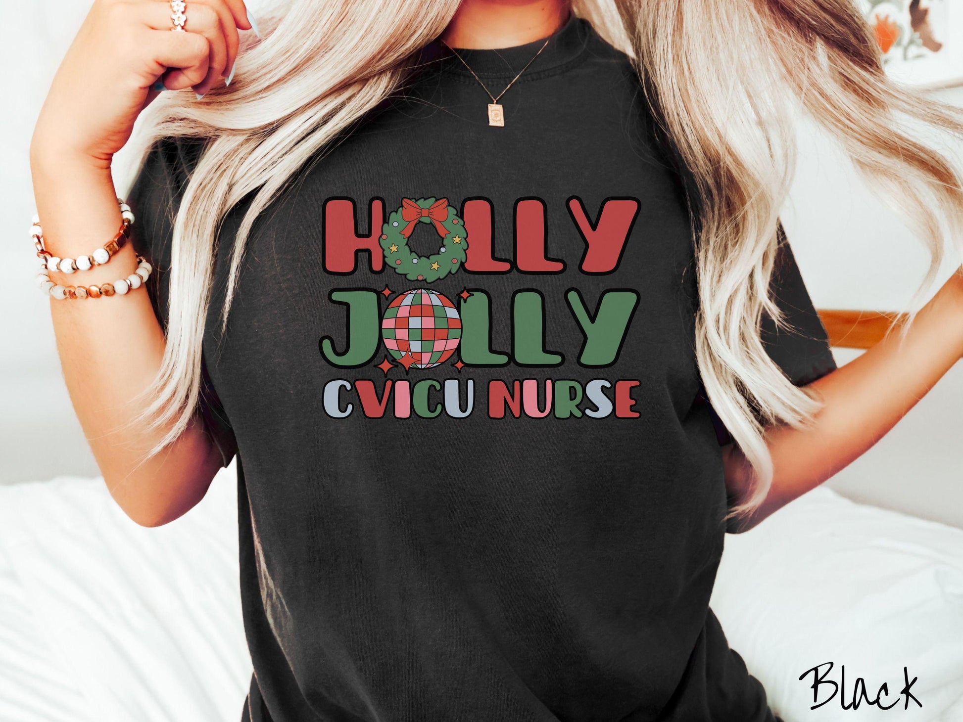 A woman wearing a cute, vintage black colored Comfort Colors T-shirt with the text Holly Jolly CVICU Nurse in red, green, pink, and blue font. The letter O in Holly is a Christmas wreath and the letter O in Jolly is a multi-colored disco ball.