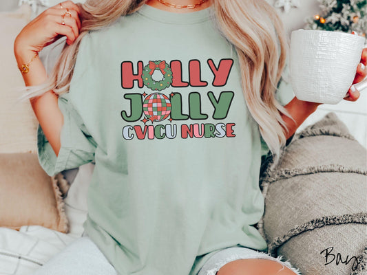 A woman wearing a cute, vintage bay colored Comfort Colors T-shirt with the text Holly Jolly CVICU Nurse in red, green, pink, and blue font. The letter O in Holly is a Christmas wreath and the letter O in Jolly is a multi-colored disco ball.