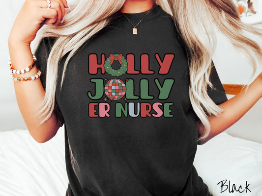 A woman wearing a cute, vintage black colored Comfort Colors T-shirt with the text Holly Jolly ER Nurse in red, green, pink, and blue font. The letter O in Holly is a Christmas wreath and the letter O in Jolly is a multi-colored disco ball.