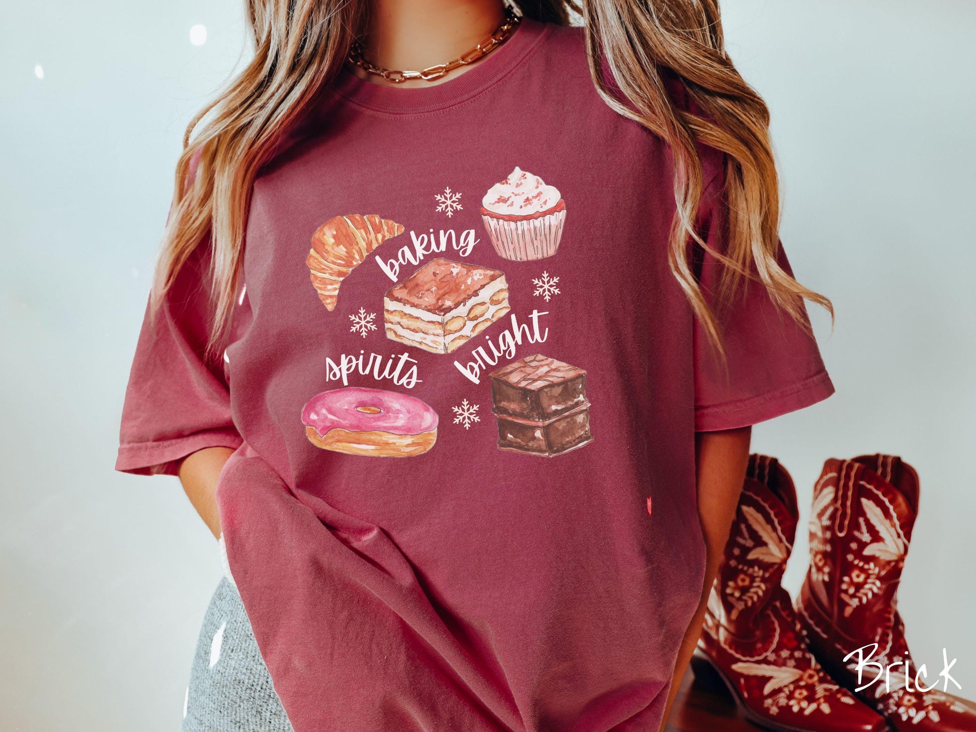This vintage brick colored Comfort Colors T-shirt features the text 'baking spirits bright' in white cursive font, accompanied by cute dessert illustrations and white snowflakes.