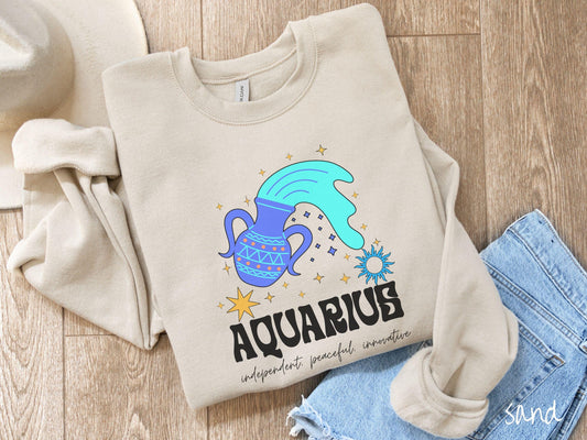 This sand colored vintage Comfort Colors sweatshirt features a large purple urn with blue water flowing out of it, surrounded by stars, with the text Aquarius and the words independent, peaceful, innovative.