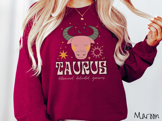 A vintage maroon colored Gildan sweatshirt features a large pink and green bull surrounded by stars and the sun with the text Taurus in large bold font and below that are the words determined, dedicated, generous in cursive font.