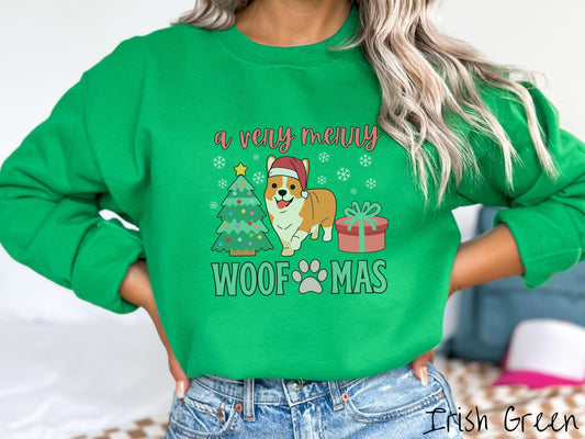 A vintage Irish green colored Gildan sweatshirt with the text &#39;a very merry Woofmas&#39; in red and green font, featuring an orange corgi wearing a red Santa hat sitting between a Christmas tree and a present with white snowflakes hanging in the air.