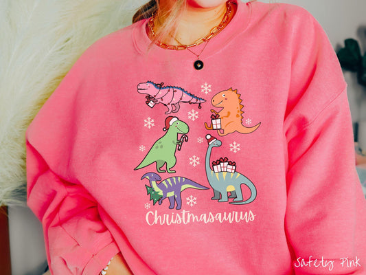 An adorable safety pink colored Christmasaurus Gildan sweatshirt. Featuring a variety of colorful dinosaurs dressed up for the holidays, this sweater exudes a playful and cheerful vibe.