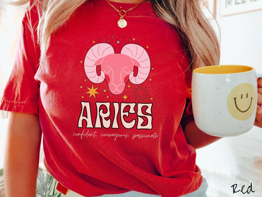 A vintage red colored Comfort Colors T-shirt features a large red ram head surorunded by stars and the sun with the text Aries in large bold font and below that ar the words confident, courageous passionate in cursive font.