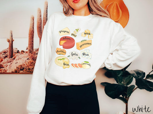 A vintage white colored Gildan sweatshirt is perfect for cheese lovers with a grid pattern of various cheeses like feta, parmesan, gruyere, goat, swiss, edam, cheddar, blue, brie, and mozzarella listed.