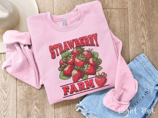 A vintage light pink colored Gildan sweatshirt featuring the text Strawberry Farm in red font with a bundle of red strawberries in between the text.