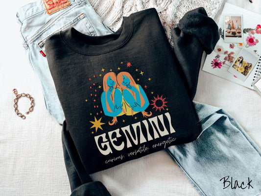 A vintage black colored Gildan sweatshirt features the twins Castor and Pollux in blue and orange colors surrounded by stars and sun with text Gemini in large bold font and below that are the words curious, versatile, energetic in cursive font.