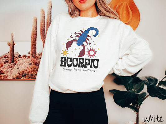 A vintage white colored Gildan sweatshirt features a large red and blue scorpion surrounded by stars and the sun with the text Scorpio in large bold font and below that are the words fearless, honest, mysterious in cursive font.