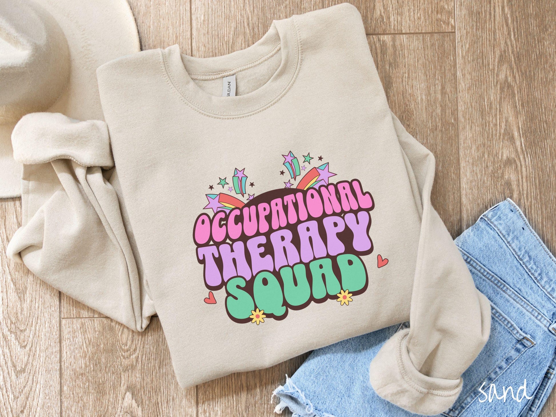 A vintage, sand colored Gildan sweatshirt with the text Occupational Therapy Squad in colorful font with red hearts, sunflowers, and shooting stars mixed in.