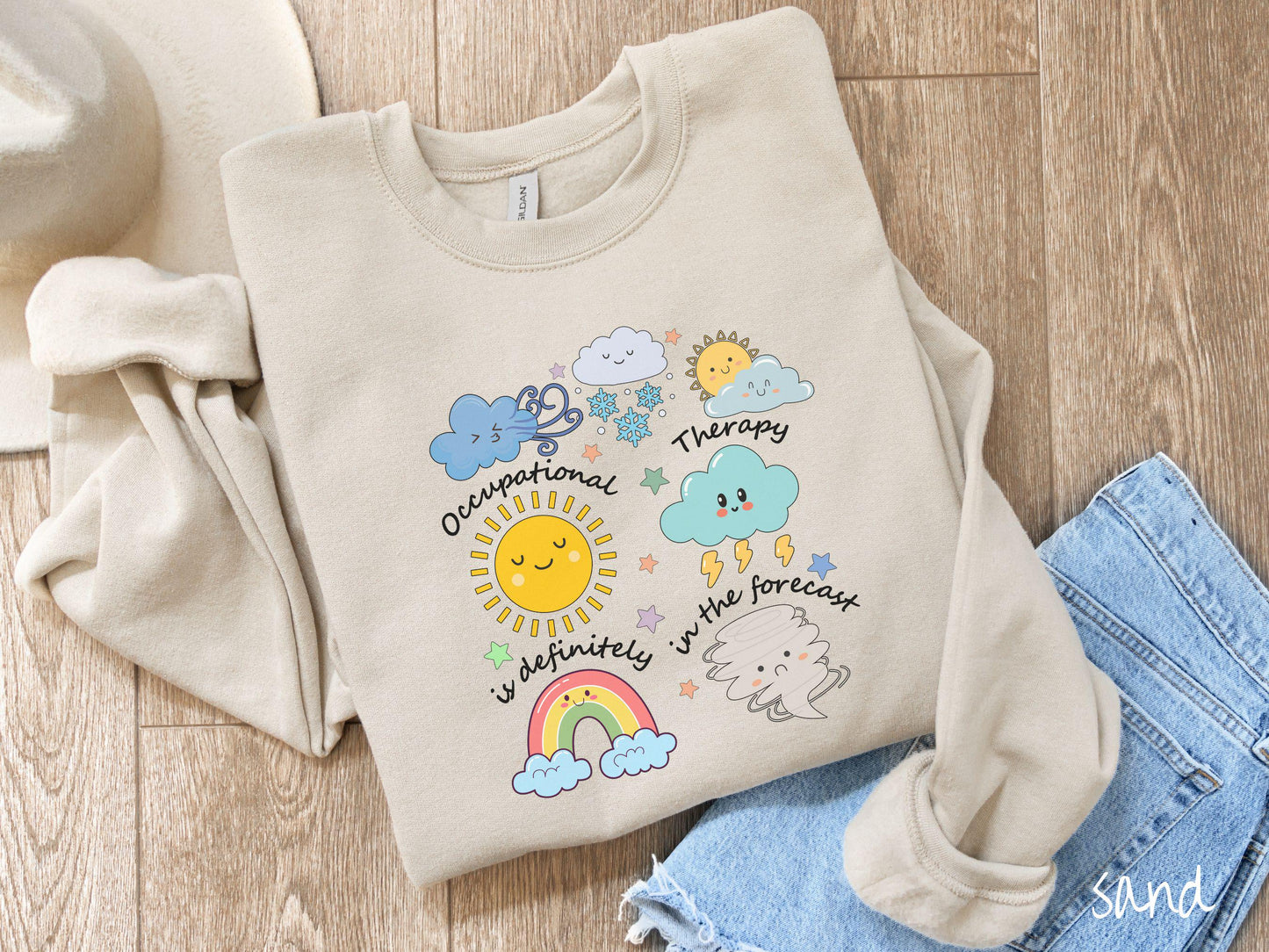 A vintage, sand colored Gildan sweatshirt featuring the text Occupational Therapy is definitely in the forecast and surrounded by weather elements like clouds, rain clouds, a shining sun, lightning, a rainbow, and a tornado.