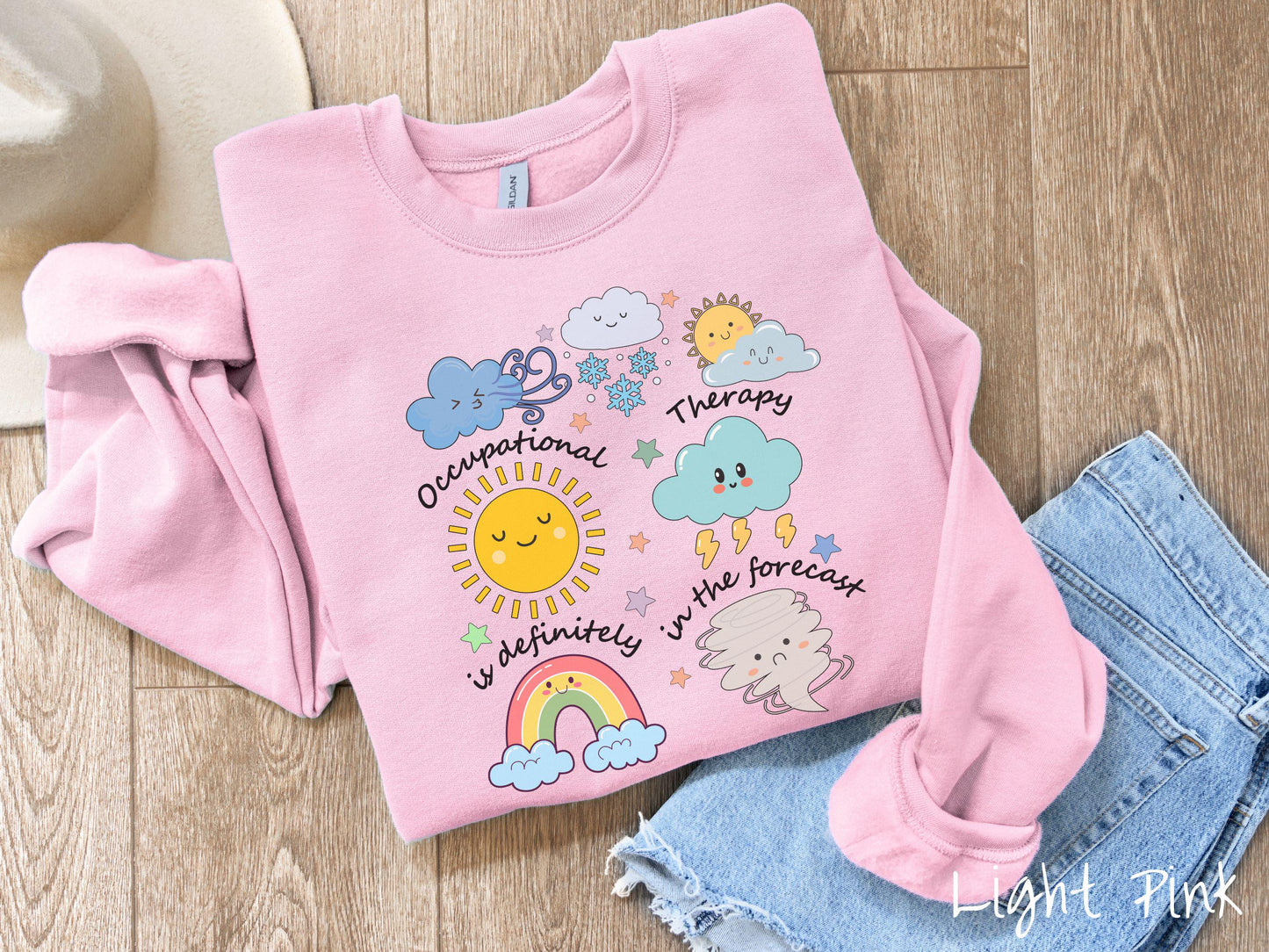 A vintage, light pink colored Gildan sweatshirt featuring the text Occupational Therapy is definitely in the forecast and surrounded by weather elements like clouds, rain clouds, a shining sun, lightning, a rainbow, and a tornado.