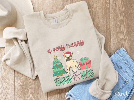 A vintage sand colored Gildan sweatshirt with the text &#39;a very merry Woofmas&#39; in red and green font, featuring a French Bulldog wearing a red Santa hat sitting between a decorated Christmas tree and a present with white snowflakes hanging in the air.