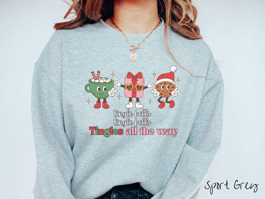 A cute, vintage sport grey colored Gildan sweatshirt with text tingle bells, tingle bells, Tingles all the way. Above are a green cup of hot cocoa, a red and pink present wearing heart-shaped glasses, and a chocolate chip cookie wearing a Santa hat.