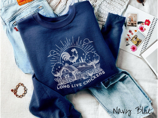 A vintage navy blue colored Gildan sweatshirt featuring a design of a farm with a fence, trees, and plants scattered along the property, a huge chicken in the background at the top of a pasture in front of the sun, and text Long Live Chickens.