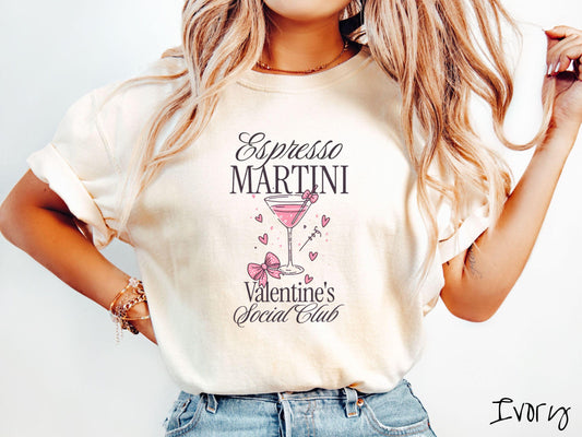 A stylish Comfort Colors T-shirt featuring the phrase &quot;Espresso Martini&quot; above a martini glass filled with pink martini a pink bow-topped toothpick. The words &quot;Valentine&#39;s Social Club&quot; appear below, with pink bows and hearts throughout the design.