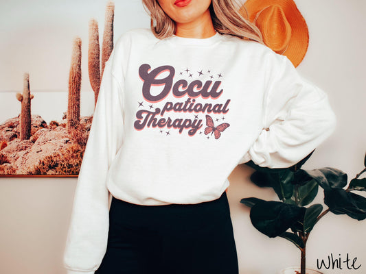 A vintage, white colored Gildan sweatshirt featuring the words Occupational Therapy across the front, this unique design showcases a stunning pink and dark purple butterfly surrounded by delicate twinkling stars.