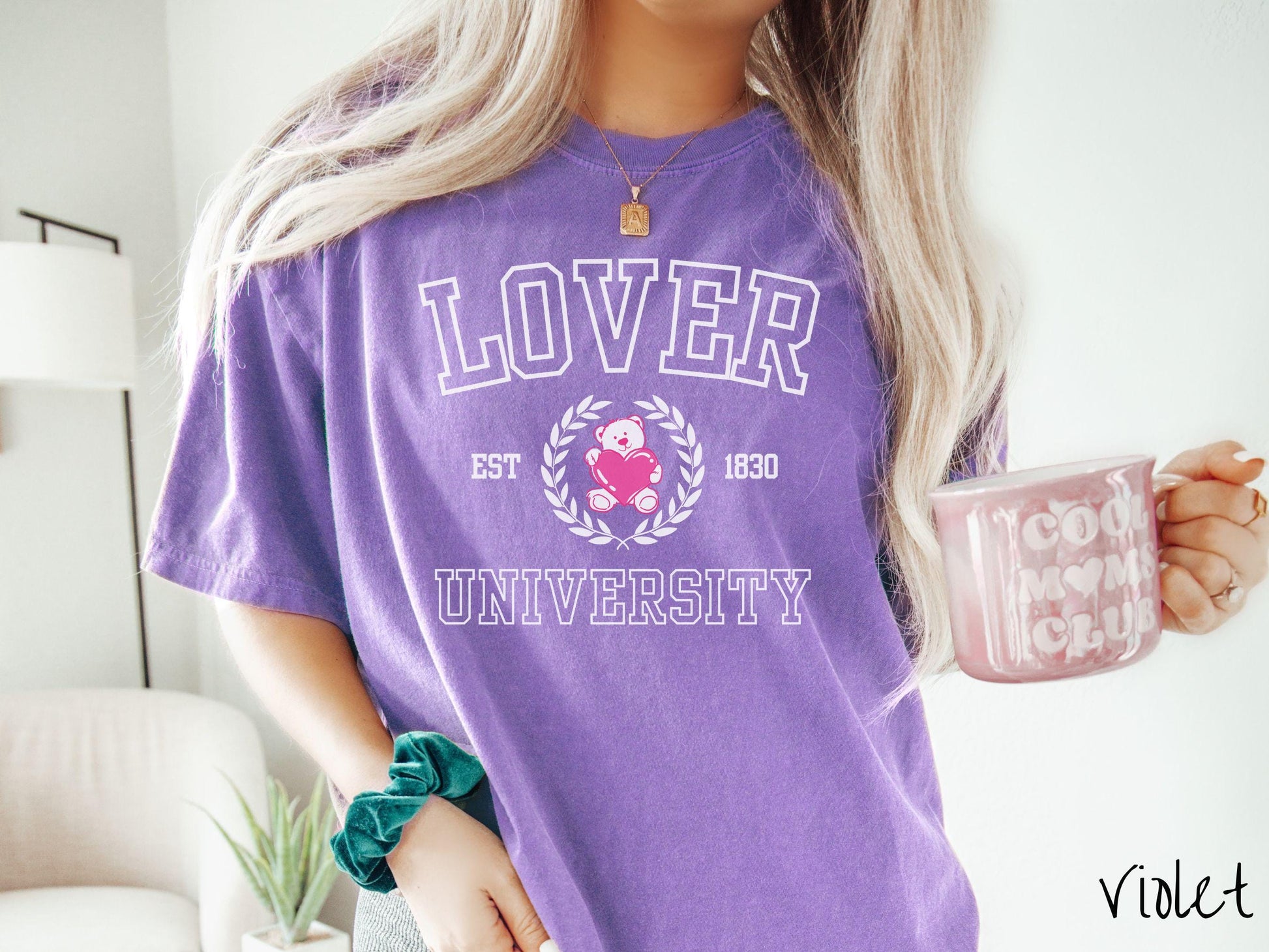 A vintage Comfort Colors t-shirt featuring a university logo-inspired design showcasing the text “Lover University” in collegiate-style font. Two pink laurel leaves frame a pink teddy bear hugging a heart with the text “EST. 1830” in pink font.