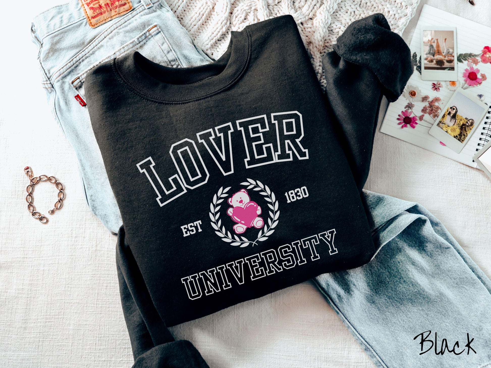 A vintage Gildan sweatshirt featuring a university logo-inspired design showcasing the text “Lover University” in collegiate-style font. Two pink laurel leaves frame a pink teddy bear hugging a heart with the text “EST. 1830” in pink font.