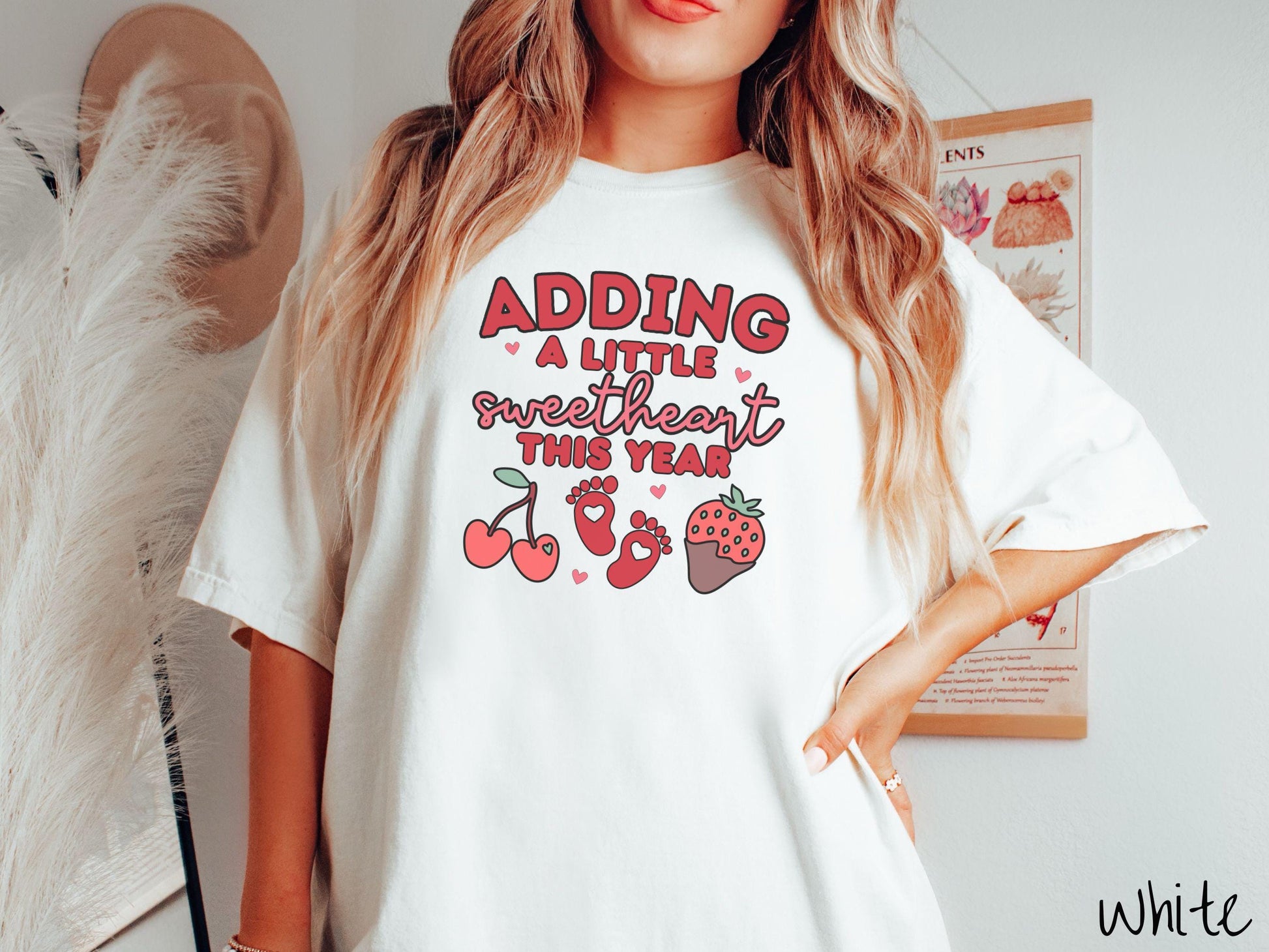 Share your exciting news with this vintage Comfort Colors t-shirt featuring the phrase “Adding a little sweetheart this year” in bold red font, paired with two red baby footprints framed by two red cherries and a chocolate-covered strawberry.