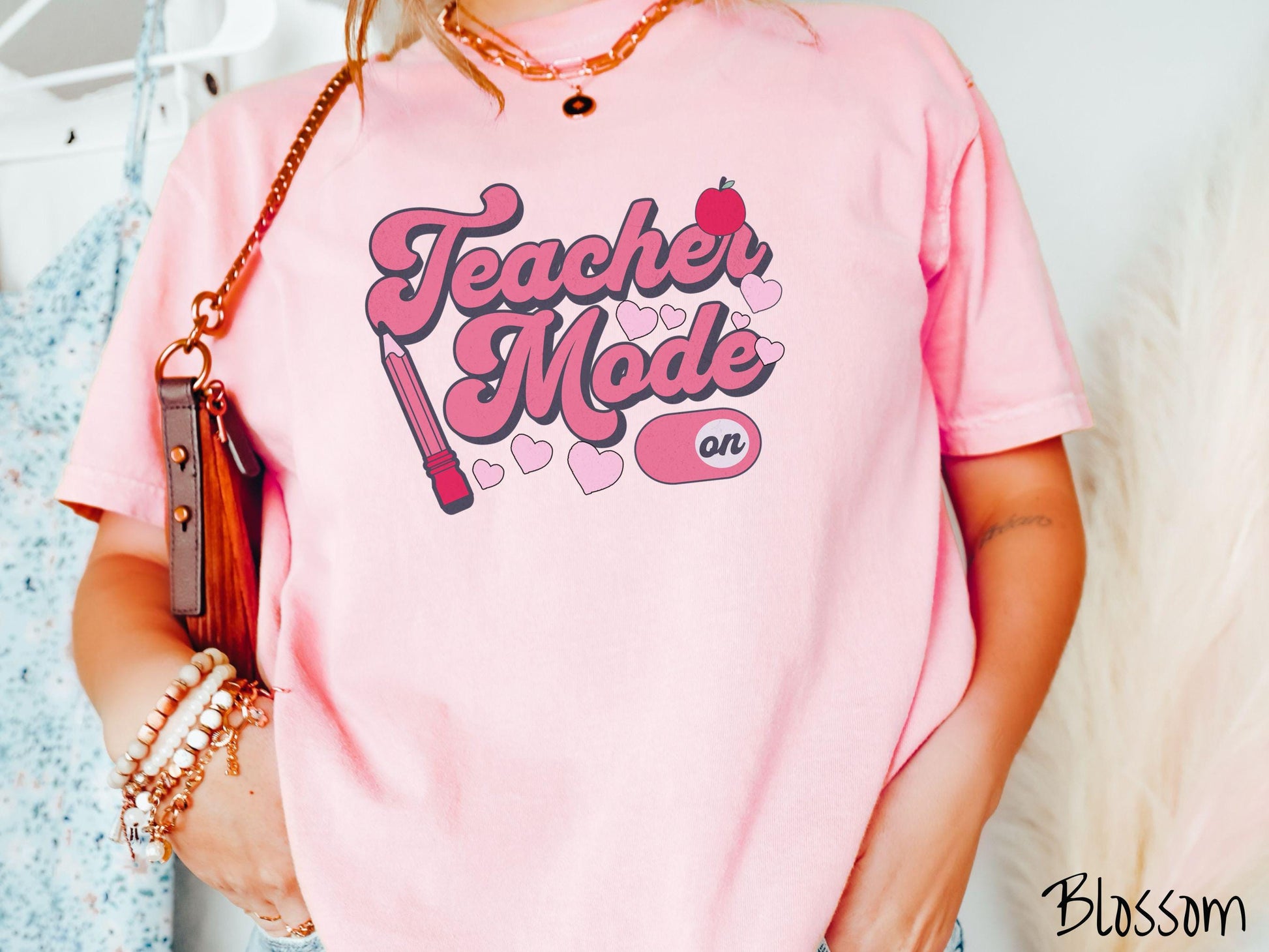 A vintage Comfort Colors t-shirt featuring the phrase “Teacher Mode” in playful pink font, an “On” button toggled to the “On” position, and with charming details like a red pencil, a red apple, and pink hearts sprinkled throughout.