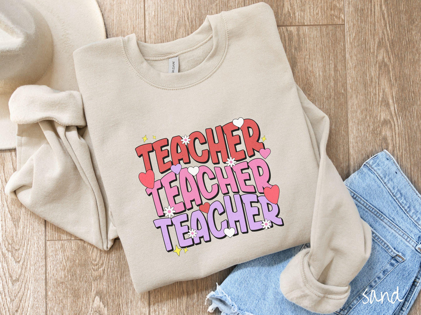 A vibrant vintage Gildan sweatshirt featuring the word “Teacher” written vertically three times in bold red, pink, and purple font, with colorful hearts, flowers, and twinkling stars scattered throughout for a whimsical and eye-catching look.