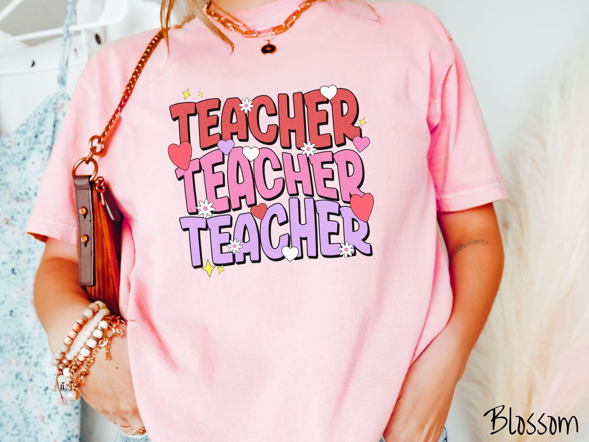 A vibrant vintage Comfort Colors t-shirt featuring the word “Teacher” written vertically three times in bold red, pink, and purple font, with colorful hearts, flowers, and twinkling stars scattered throughout for a whimsical and eye-catching look.