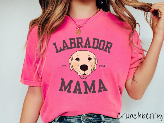 A vintage Comfort Colors t-shirt featuring bold block lettering that reads &#39;Labrador Mama.&#39; At the center of the design, a playful yellow Labrador with its tongue out steals the spotlight, framed by the stylish text &#39;EST. 2024.&#39;