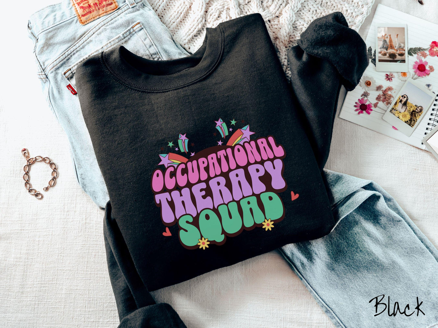 A vintage, black colored Gildan sweatshirt with the text Occupational Therapy Squad in colorful font with red hearts, sunflowers, and shooting stars mixed in.