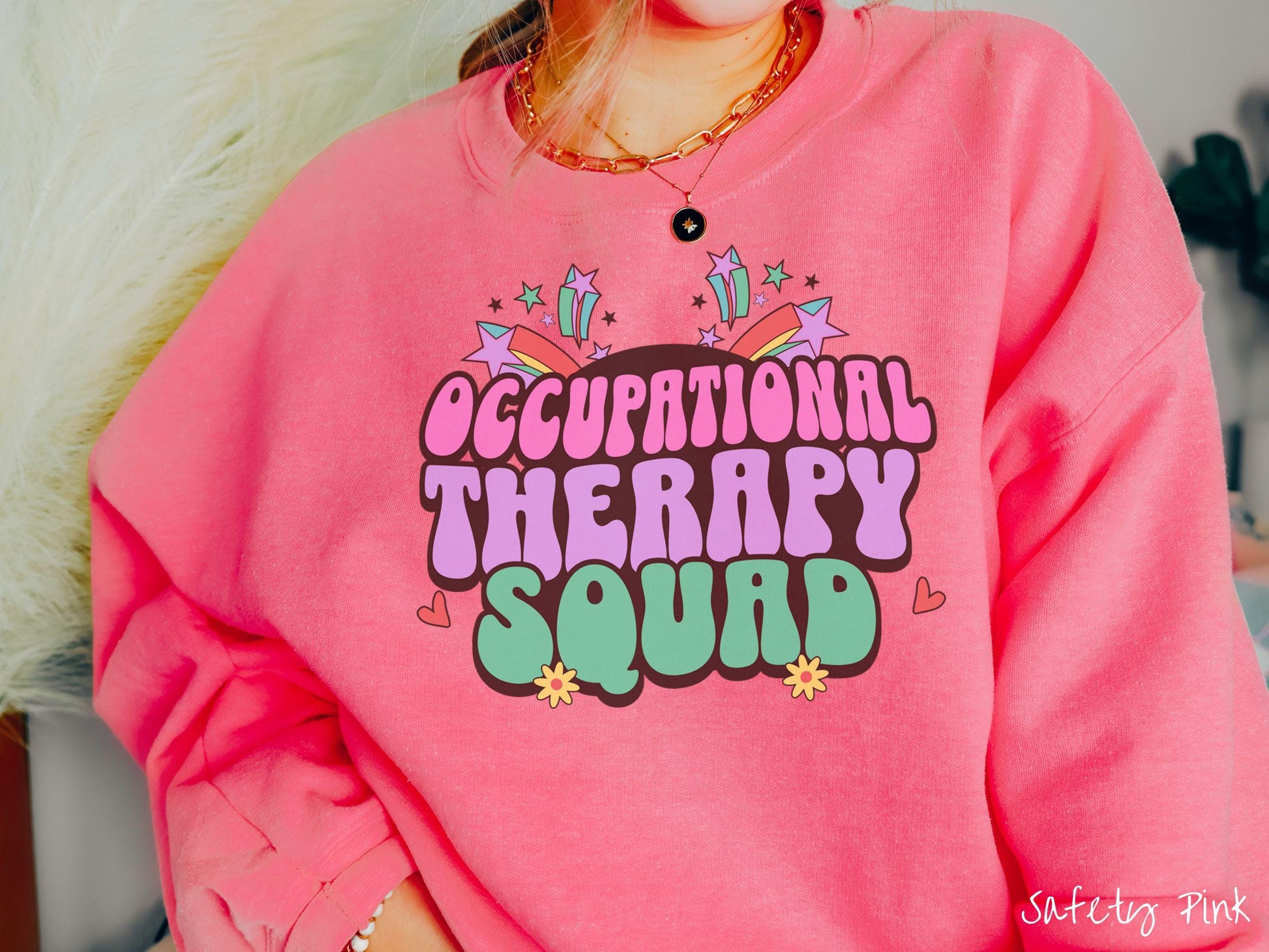 A vintage, safety pink colored Gildan sweatshirt with the text Occupational Therapy Squad in colorful font with red hearts, sunflowers, and shooting stars mixed in.